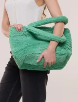 Cartera tipo shopper verde de textura suave y flexible, con doble asa superior fija texturada y compartimento principal amplio con botón metálico.