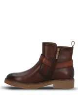 Botines de cuero color marrón oscuro, con diseño de caña media, cierre lateral y una tira decorativa con hebilla metálica sobre el empeine. Presentan una suela de goma texturizada en tono natural y un pequeño logo metálico en la parte superior de la caña.