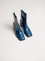 Botas de cuero color marrón con caña media y punta cuadrada. Presentan un cierre trasero, tirador para calzar fácilmente y bordado en color contrastante en el empeine. Suela de goma y taco de madera de 6 cm de altura.