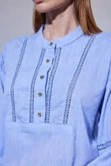 Camisa blanca de algodón con pechera decorada con alforzas y puntillas. Presenta cierre frontal con botones, mangas tres cuartos con frunces y detalles de puntilla, y un diseño de corte holgado con ruedo redondeado.