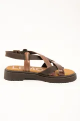 Sandalias de cuero color marrón con suela track, tiras cruzadas en el empeine con diferentes texturas y acabados, y tira ajustable al tobillo con hebilla metálica.