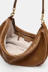 Bolso de hombro de diseño slouchy en color marrón, con asa de hombro ajustable mediante mosquetones metálicos dorados y cierre superior de cremallera.