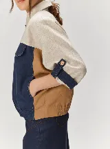 Chaqueta de lino de corte holgado con diseño en bloques de color beige, negro y tostado. Presenta cierre frontal de botones, cuello camisero, bolsillos con solapa en el pecho y mangas con presillas para ajustar.