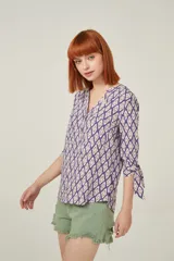 Blusa de viscosa con estampado geométrico en tonos violeta y beige. Tiene cuello mao, botones frontales y mangas 3/4 con lazo en los puños.