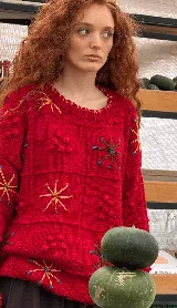 Buzo tejido a mano en lana merino, de corte oversized y diseño en bloques. Presenta un vibrante color rojo con detalles bordados a mano en forma de flores y texturas en relieve.