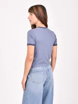 Remera ajustada color azul grisáceo, con cuello redondo y ribete en contraste en el cuello y las mangas. Presenta un estampado frontal con texto que dice "Beverly Hills Tennis Club Est. 1985" y un gráfico de una raqueta de tenis y una copa de vino cruzadas.