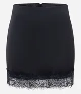 Short pollera de satén negro con acabado brillante, corte ajustado y detalle de encaje floral con transparencia en el ruedo. Cuenta con cierre invisible en la parte trasera.