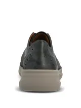 Zapato estilo oxford con cordones de cinta, confeccionado en una combinación de gamuza y cuero con detalles perforados tipo brogue. Presenta una suela de plataforma plana en color gris claro.