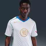 Camiseta deportiva Nike Total 90 Energy de manga corta, color blanco con detalles en dorado, verde, azul y rojo. Presenta un diseño de paneles curvos, cuello en V tricolor y el gráfico distintivo '90' en el centro del pecho.
