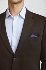 Blazer de corte clásico color azul oscuro, con cierre frontal de un botón, solapas de muesca y bolsillos laterales con solapa. Presenta un bolsillo superior con pañuelo decorativo y puños con botones.