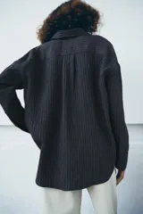 Camisa fluida de corte oversize confeccionada en mezcla de viscosa, con diseño de rayas verticales finas en tono beige sobre fondo blanco. Presenta cuello solapa, cierre frontal con botones, manga larga con puños y un bolsillo de plastrón en el pecho.