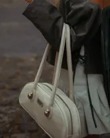 Cartera baguette de cuero marrón con manijas largas y detalle de nudos esféricos de alpaca en la unión de las manijas.