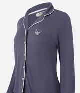 Pijama de dos piezas estilo americano en color azul grisáceo. La blusa es de manga larga con cuello solapa, cierre frontal de botones y detalle de bies en contraste. El pantalón es de corte recto con cintura elástica y detalle de bies en el ruedo.