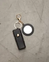 Llavero negro con espejo circular y estuche para labial con tachas doradas.