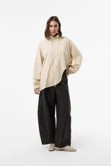 Buzo de punto oversize en color beige, con capucha, cordones largos ajustables y mangas largas amplias con puños elásticos. Presenta diseño asimétrico, más largo en la parte posterior.