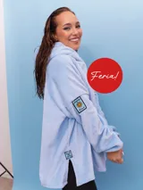 Buzo oversize celeste de terciopelo, con capucha, mangas largas y aberturas laterales en el ruedo. Cuenta con un parche decorativo bordado en la manga y otro en la parte inferior.