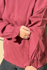 Blusa de algodón color bordó, con diseño de volados en los hombros, mangas largas con puños elásticos y corte holgado.
