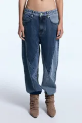Pantalón de jean con diseño de patchwork que combina diferentes tonos de denim en paneles geométricos. Presenta un corte relajado, tiro medio y cierre frontal con botón metálico.