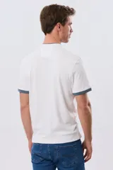 Remera blanca de manga corta con cuello mao y cierre frontal parcial con tres botones. Presenta detalles en color azul en el cuello y en los bordes de las mangas, además de un pequeño logo bordado en el pecho.