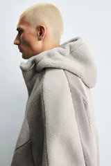 Cazadora de corte relajado confeccionada en tejido con textura efecto borreguillo. Presenta un diseño bicolor con capucha ajustable, cierre frontal con cremallera, bolsillos laterales y puños elásticos.