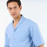Camisa de manga corta de mezcla de lino en color celeste, con cuello cubano, cierre frontal con botones y un bolsillo aplicado en el pecho.