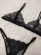 Conjunto de lencería de encaje negro, compuesto por un soutiene tipo triángulo con tirantes finos regulables y una bombacha cavada con tiras laterales regulables.