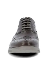 Zapato tipo Oxford con diseño brogue, confeccionado en cuero color marrón oscuro. Presenta cordones al tono y una suela de goma gris con diseño deportivo.