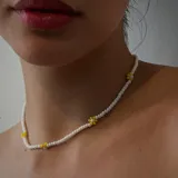 Gargantilla de cuentas pequeñas color blanco, con apliques de flores amarillas.