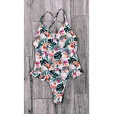 Malla enteriza blanca con estampado de hojas y flores en tonos naranja, verde, rosa y negro. Tiene breteles finos cruzados en la espalda y volados en la parte inferior.