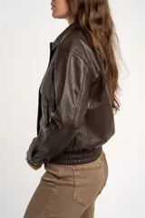 Campera bomber de cuero sintético marrón, con cierre frontal, cuello camisero, bolsillos laterales y elástico en los puños y la cintura.