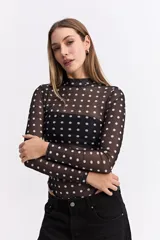 Body de manga larga confeccionado en tejido mesh transparente con estampado de lunares blancos sobre fondo negro. Presenta cuello alto y un diseño ajustado al cuerpo.