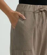 Pantalón estilo jogger de suedine, con cintura elástica y cordón ajustable, puños elásticos en los tobillos, bolsillos laterales y detalles perforados en los laterales y bolsillos.