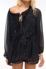 Blusa negra traslúcida con mangas largas abullonadas y detalle de encaje floral en el frente.