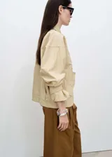 Campera color beige, tipo anorak, con cuello camisero, cierre frontal con botones, manga larga con trabillas, diseño oversize y forro interior.