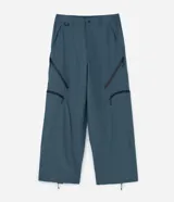 Pantalón de corte holgado en color azul petróleo, confeccionado en microfibra de poliéster. Presenta un diseño utilitario con múltiples bolsillos funcionales, cierres visibles y detalles técnicos en las piernas.