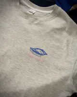 Remera oversize gris melange de manga corta, con estampa en la espalda de caracoles marinos en tonos azules y texto en rosa.