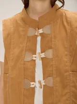 Chaleco color tostado de lino y algodón, con cuello mao y cierre frontal con alamares. Posee bolsillos frontales aplicados y costuras pespunteadas a contratono.
