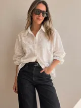 Camisa oversize color marfil, de manga larga y calce amplio, confeccionada con detalles de bordados en relieve en todo el diseño. Cuenta con cuello clásico, cierre frontal con botones y ruedo asimétrico, más largo en la parte trasera.