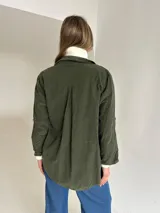Camisa de pana en color verde oscuro, con corte oversize, cuello clásico, cierre frontal de botones y bolsillos delanteros. Cuenta con mangas largas con detalle de botón para ajustar.