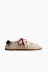 Calzado deportivo de gamuza color beige, con cordones intercambiables en tonos blanco y bordó, detalle de talón plegable con refuerzo negro y suela plana de goma acanalada.