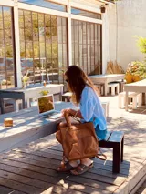 Mochila de cuero marrón con cierre superior y múltiples bolsillos externos. Se puede convertir en bolso de mano o bandolera gracias a sus correas ajustables y extraíbles.