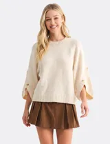 Buzo de punto beige con mangas tres cuartos anchas, cuello redondo y detalle de botones en las mangas.