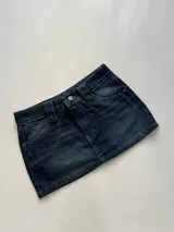Minifalda de jean azul con lavado oscuro, corte ajustado, tiro bajo y diseño de cinco bolsillos con costuras reforzadas.