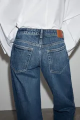 Jeans de mezclilla en color negro gastado, tiro bajo, corte de pernera recta y diseño clásico de cinco bolsillos con cierre frontal de cremallera y botón metálico.