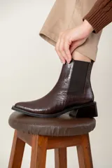 Bota tipo chelsea de caña media con acabado efecto cocodrilo en color chocolate. Presenta paneles elásticos laterales, puntera cuadrada y taco ancho geométrico.