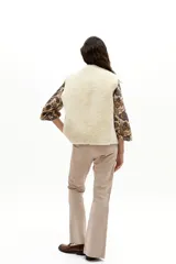 Chaleco reversible de gamulán de oveja color marrón tostado, con interior de piel sintética blanca, cuello a la base y cierre frontal mediante tiritas de cuero para atar.