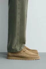 Zapato de cordones con parte superior de piel con acabado serraje, detalle de bordón en el empeine, horma redonda y suela a tono con piso track.