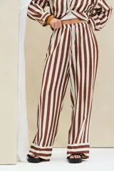 Pantalón largo de corte ancho, con diseño de rayas verticales en colores marrón y blanco, cintura elástica con cordón de ajuste y detalles de franjas horizontales en el ruedo.