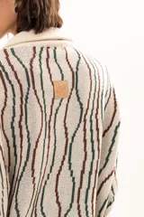 Buzo de tejido de punto con diseño de rayas verticales onduladas en tonos verde y marrón sobre base color crudo. Presenta cuello tipo polo con cierre frontal de botones y mangas largas con puños acanalados.