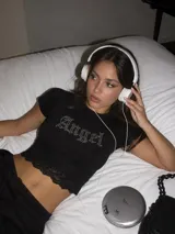 Remera negra corta de manga corta, con el texto "Angel" en pedrería en el pecho y detalle de encaje negro en el borde inferior.